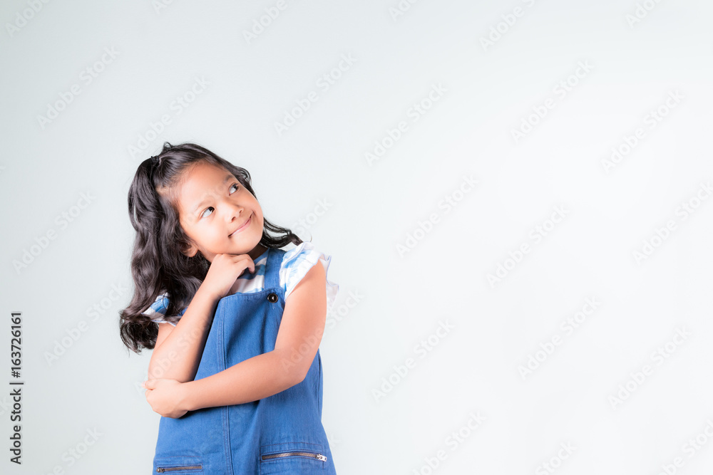 young asian little girl in blue jeans dungarees thinking and looking up with white concrete wall background... young asian little girl in blue jeans dungarees thinking and looking up with white concrete wall background...