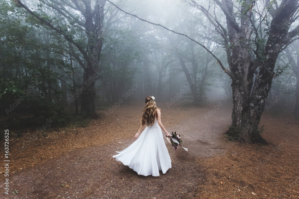 Bride whirls in light dress in the beautiful fairy forest. Foggy autumn weather Bride whirls in light dress in the beautiful fairy forest. Foggy autumn weather
