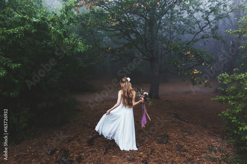 Bride whirls in light dress in the beautiful fairy forest. Foggy autumn weather