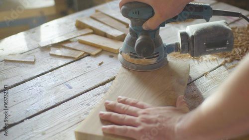 Hands of woodworker carpenter grinding wooden plank in backlight using machine