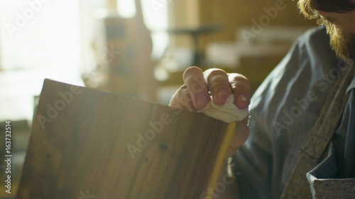 Close up hands of carpenter woodworker rubs lacquer on a wooden plank