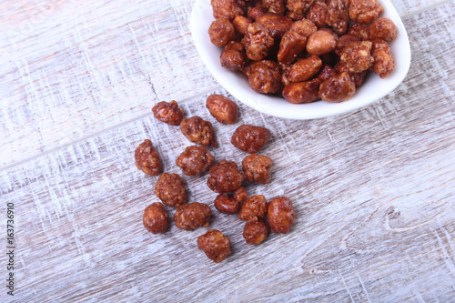 Sugared Hazelnuts in a white bowl on a wooden background. Hazelnuts in sugar glaze. Selective focus.