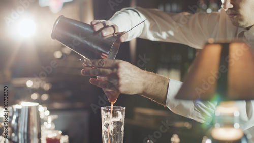 Bartender in hat is preparing cocktail in bar