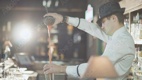 Bartender in hat is preparing cocktail in bar