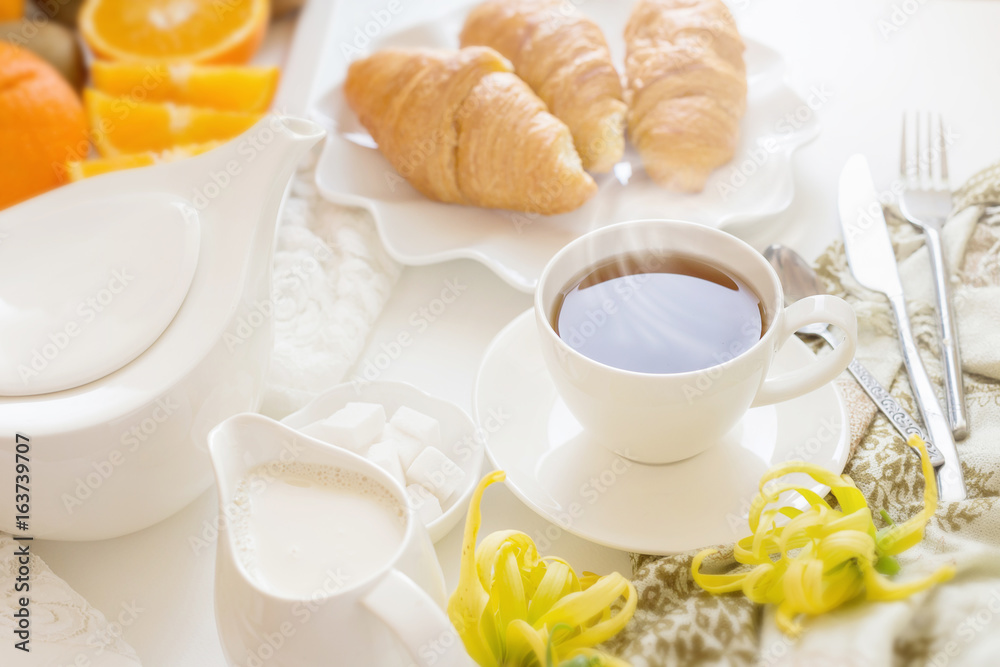 Continental breakfast with gold french croissants fruits and cup of tea on white table in a Morning light. Breakfast concept