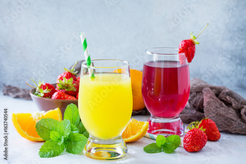 Refreshing summer drinks assortment. Orange juice, strawberry juice, fresh oranges and strawberries on a gray stone or slate background.