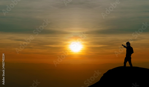 Silhouette man stand on the rock and point the Sunset in mountain © momolelouch