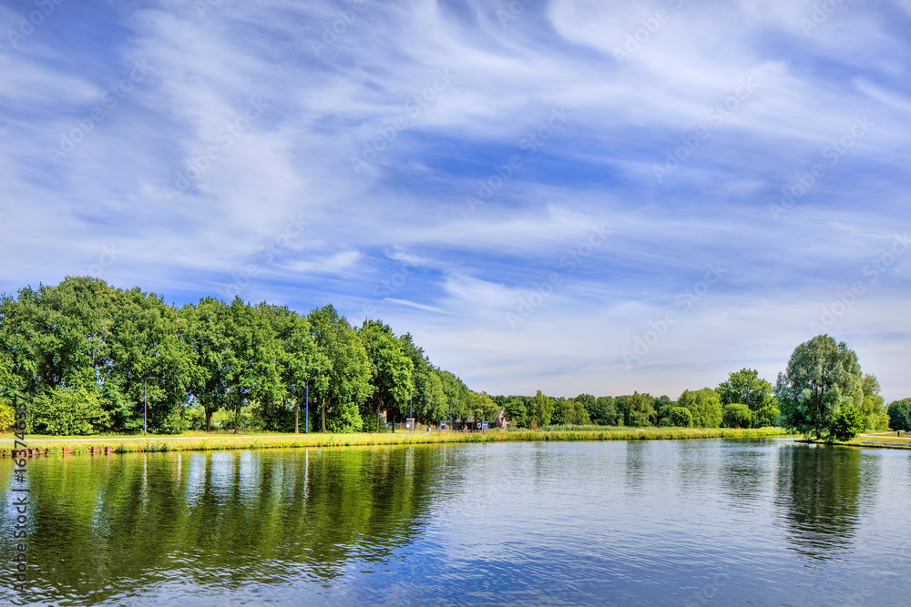 Fototapeta premium Tranquil landscape with a canal, trees, blue sky and dramatic cloud formation.
