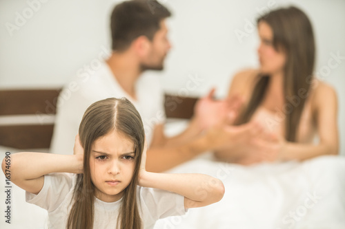The unhappy girl sitting near the arguing parents on the bed