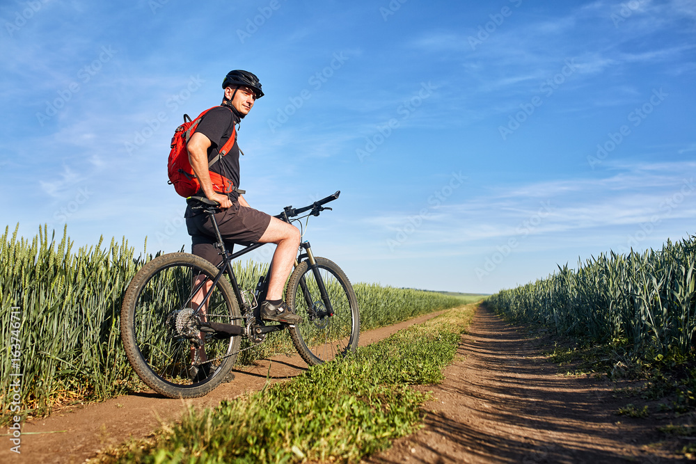 Attractive one cyclist on mountainbike on path near green fields in the countryside in the summer season.