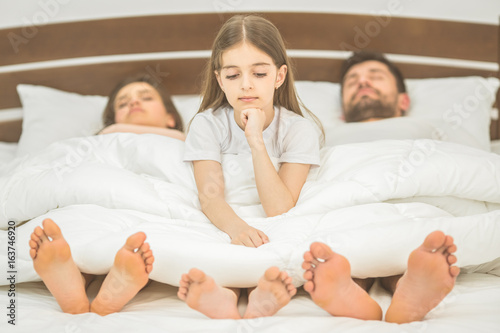 The little girl sit near the parents in the bed