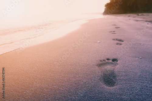 Foot print on the beach on sunrise sea background with vintage filter photo