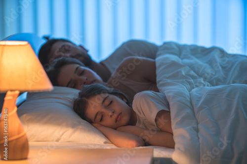 The little girl sleeping near the parents in the bed. night time