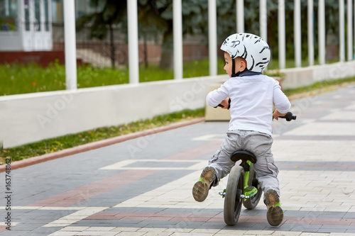 Child boy in white helmet riding on his first bike with a helmet. Bike without pedals.