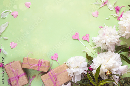 White peonies with gift boxes and decorative hearts on green background. Copy space. © WindyNight
