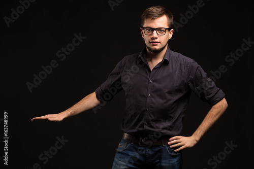 Young confident man showing by hands on a black background. Ideal for banners, registration forms, presentation, landings, presenting concept.