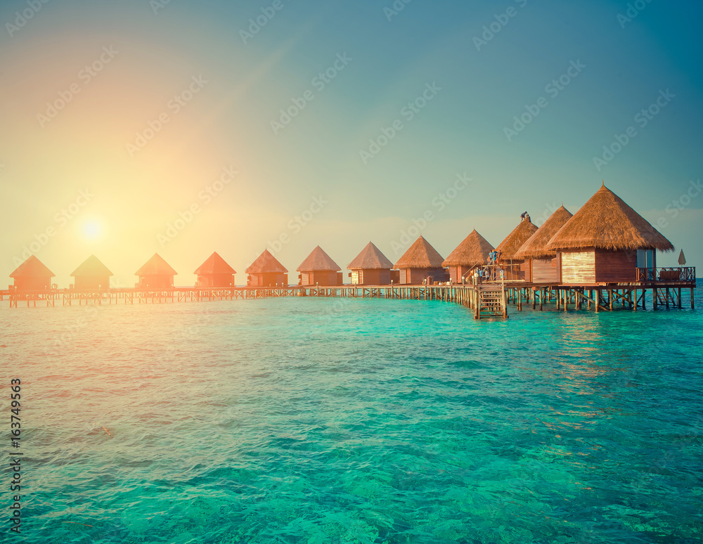 houses over the transparent quiet sea water  on a sunset , toning. Maldives