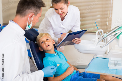 Dentist man with assistant are diagnosticating to young patient which is sitting