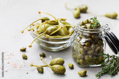 Mixed capers in jar and bowl on white kitchen table. photo