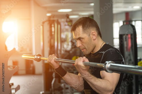 Strong man exercising with a barbell in a gym with sunlight