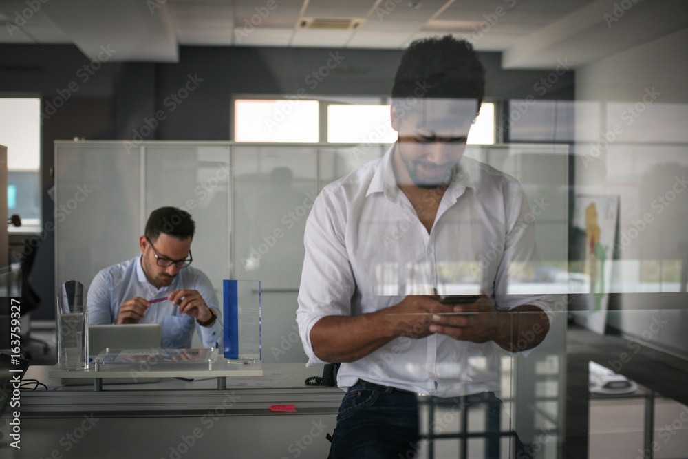 African American business person standing in office and using smart phone. African American business person standing in office and using smart phone.
