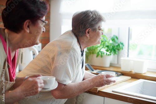 Senior adult women drinking coffee and peering out of window