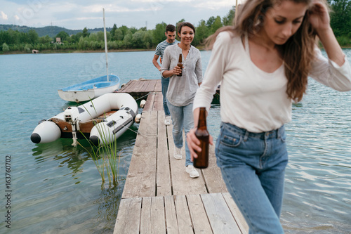 Three friends walking along pier, holding bottled beer