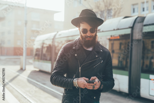 Young male hipster looking at smartphones  at city tram station photo