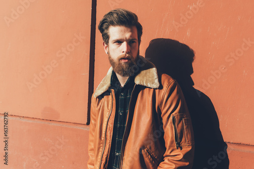 Portrait of cool young bearded man leaning against orange wall photo