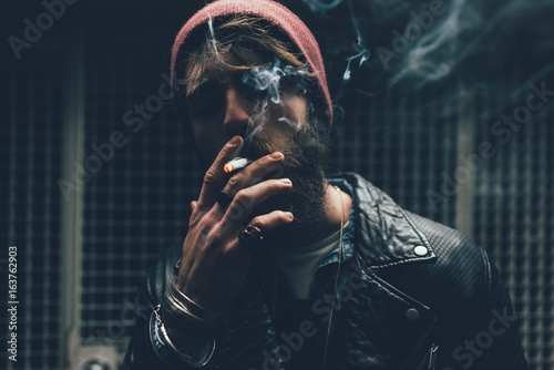 Young male hipster smoking cigarette in dark city doorway at night photo