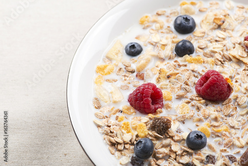 Plate of cereals with milk, raspberries and blueberries.