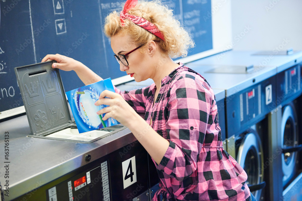 Woman inserting washing powder into washing machine at laundrette Stock