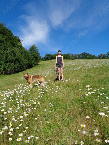 Girl with dog on chamomile field, green trees and blue sky