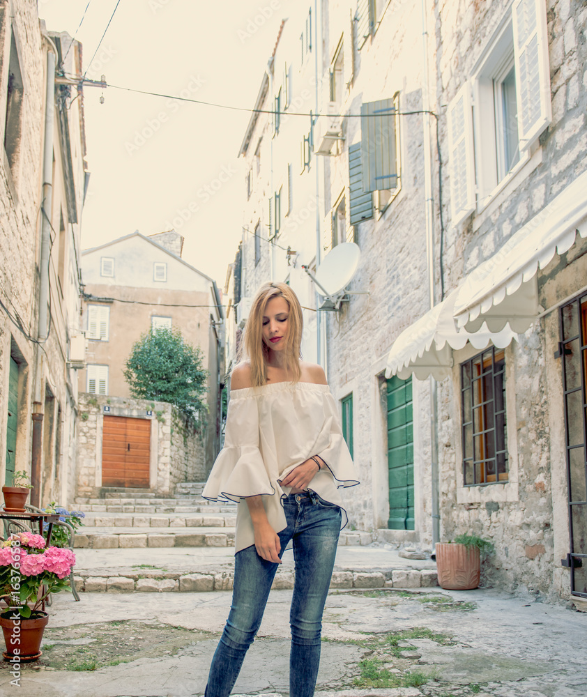 Outdoor portrait of model woman in fashionable white blouse and blue jeans.City lifestyle.Concept of Women fashion in retro and vintage.