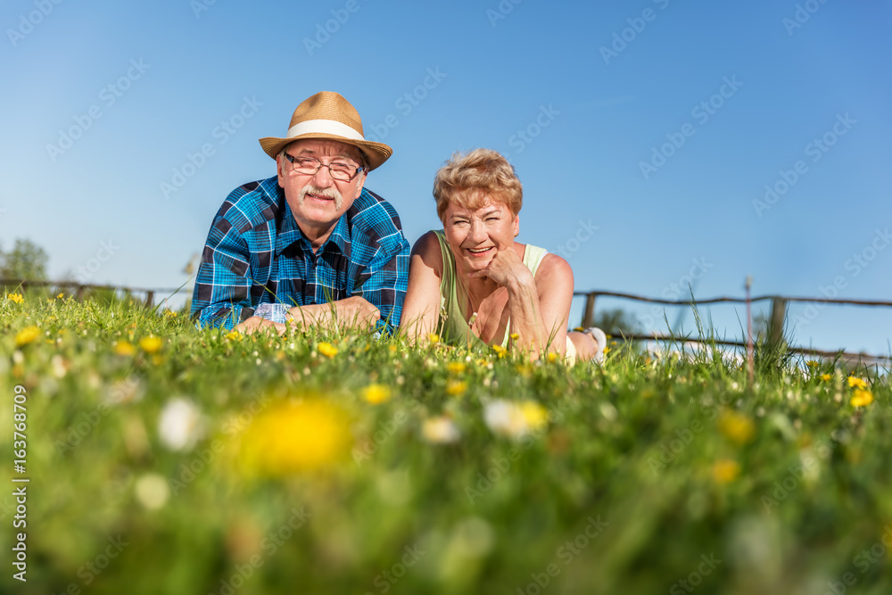 Senior couple lying on the summer field in green grass Senior couple lying on the summer field in green grass
