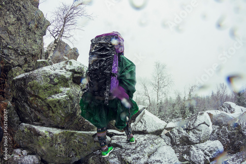 Rear view of female hiker in waterproof clothing looking out from mountain in snowstorm photo