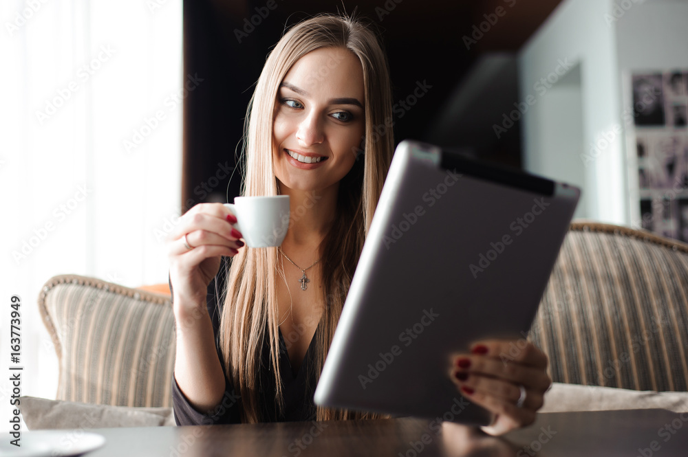 Businesswoman drinking coffee, tea in a coffee shop using a tablet Businesswoman drinking coffee, tea in a coffee shop using a tablet