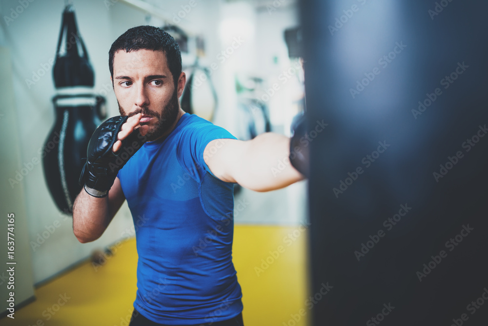 Young muscular kickboxing fighter practicing kicks with punching bag.Boxing on blurred background.Concept of a healthy lifestyle.Horizontal.