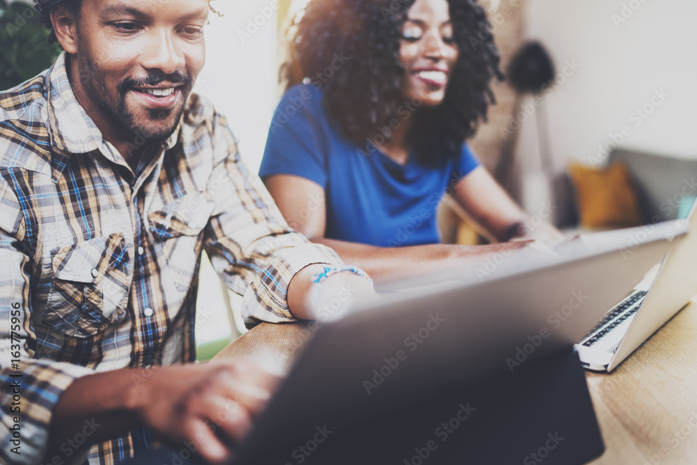 Young smiling african american couple working together at home.Young black man and his girlfriend using laptop and touch tablet at home in the living room. Horizontal,blurred background.Cropped.