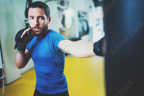 Young boxer man doing some training on punching bag at gym. Bearded caucasian boxer training with punching bag in gym.Concept of a healthy lifestyle.Horizontal.
