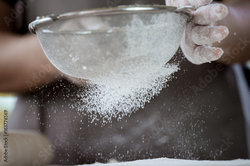 Woman prepare bread dough, spreading the flour through a sieve on dough for baking cookies in the kitchen in vintage color tone photo