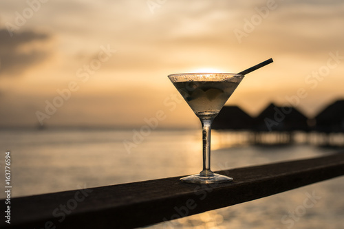Cocktail glass on wooden rails overlooking the sea. When the sun is falling