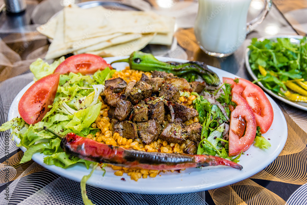 Close up detailed view of grilled delicious liver Turkish shish kebab served on a white plate with sliced lavash,parsley,onion,lettuce,tomatoes ,grilled pepper,mixed pickles and ayran.