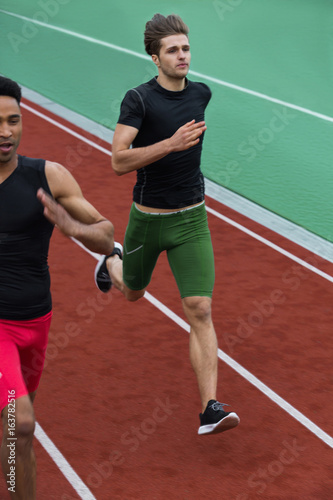 Handsome multiethnic athlete group run on running track © Drobot Dean