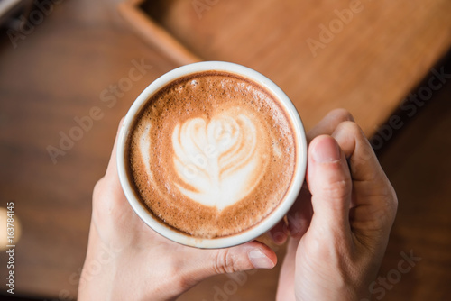 Women holding a hot cup of coffee in hands in coffee shop .