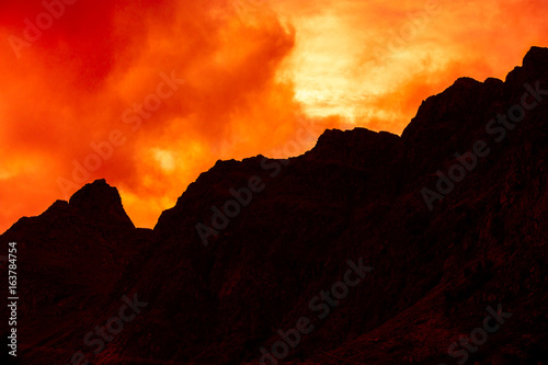 Mountain top outlined with cloudy sunset sky. Burned red sunset. Beautiful nature Norway. Lofoten islands. Reine