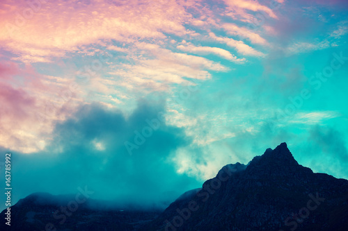 Mountain top outlined with cloudy sunset sky. Pink yellow sunset. Beautiful nature Norway. Lofoten islands. Reine