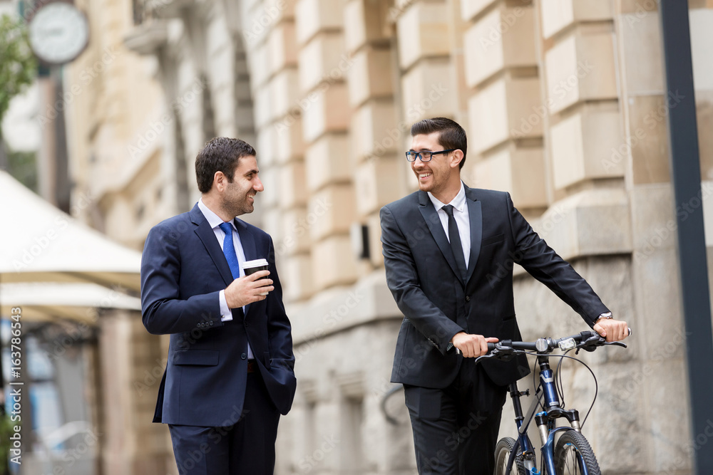 Two young businessmen with a bike in city centre Two young businessmen with a bike in city centre