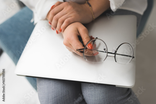 cropped view of female hands with laptop and eyeglasses in office
