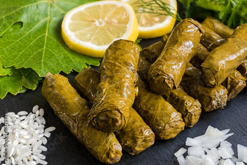 Delicious stuffed grape leaves (the traditional dolma of the mediterranean cuisine) on black dish with leaves, lemon slices, rice, parsley, dill and onion photo